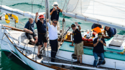 a sailing boat with some male sailors on it, waving upwards