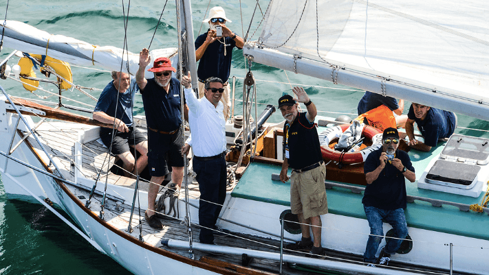 a sailing boat with some male sailors on it, waving upwards
