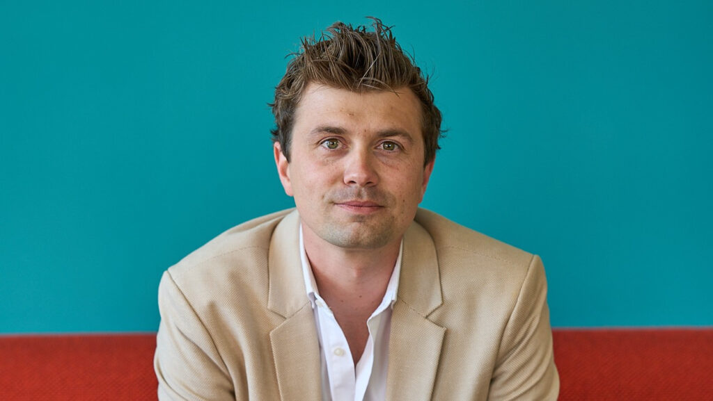 man, wearing beige jacket, smiles at camera. This is Conrad Empson
