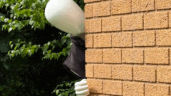 a faceless mannequin peers around a corner of a brick wall