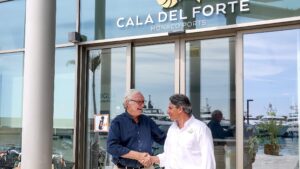 Two men shake hands at under Cala del Forte sign and office front
