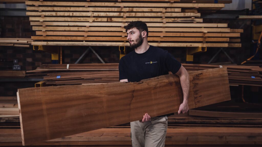 Male boatbuilder carries wood at Spirit yachts
