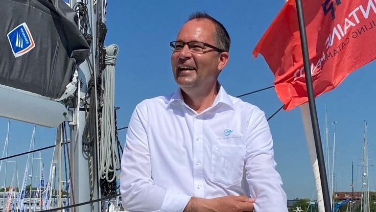 Man in suit shirt and trousers smiling on a yacht