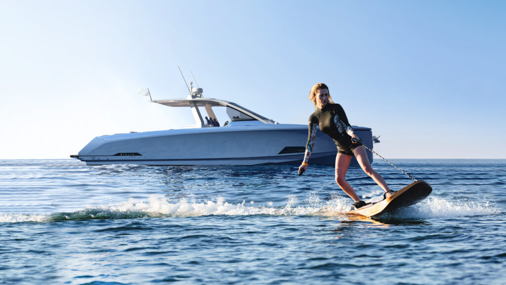 A small white power boat in background with woman on electric board in foreground