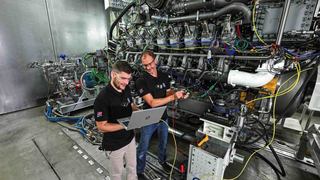 two men in safety goggles testing large marine methanol engine in factory