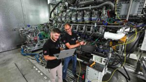 two men in safety goggles testing large marine methanol engine in factory