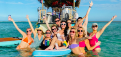 A bevvy of party-goers stand in front of a boat in the sea to show that boat rental is fun