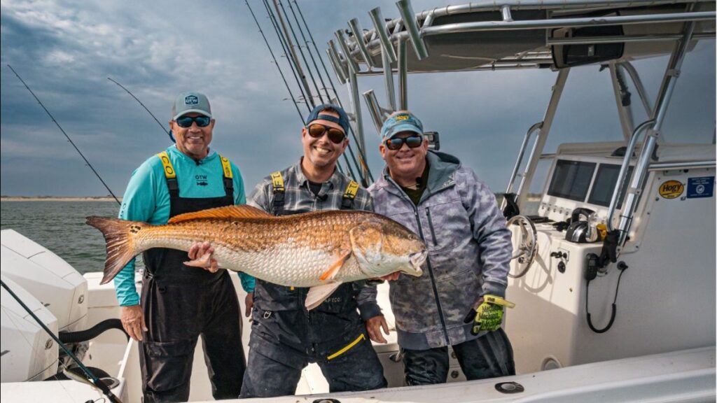 three men holding a large orange fish on a sportfishing boat