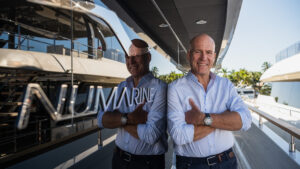 man smiling standing on the side deck of a black shiny boat