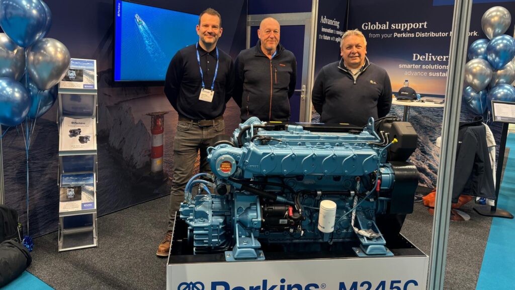 Three men standing by a marine engine at exhibition