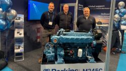Three men standing by a marine engine at exhibition