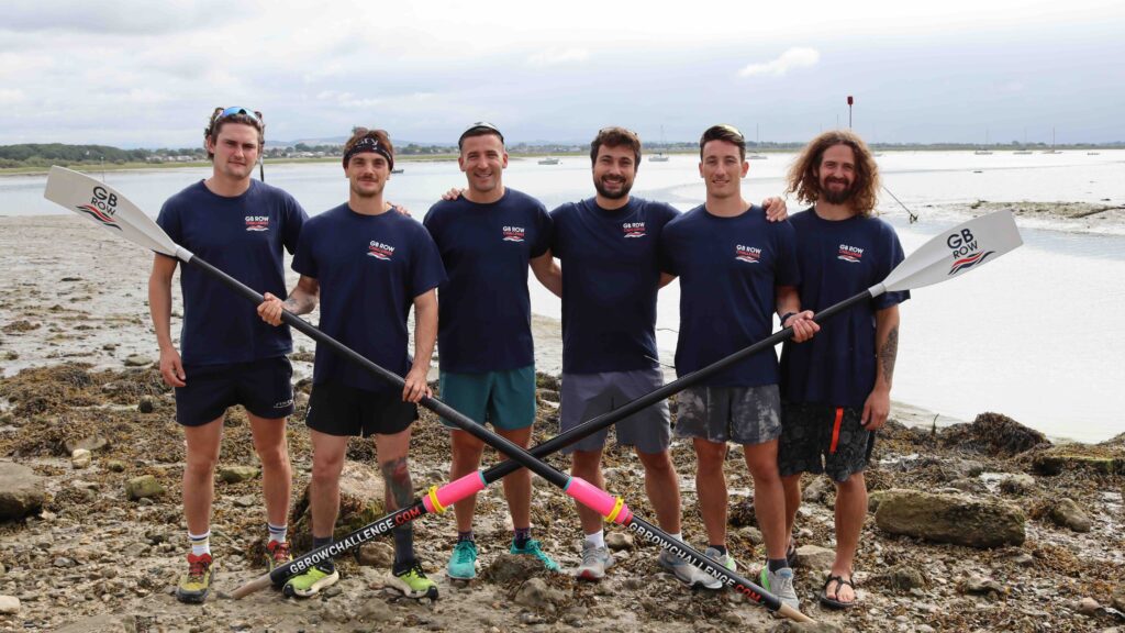 Team of six rowers holding two oars on beach