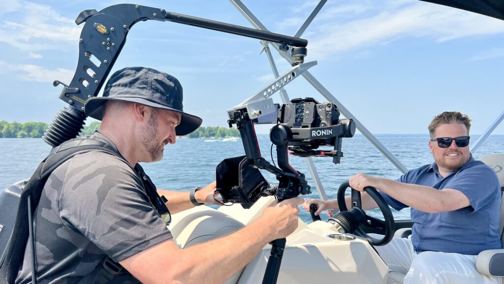 One man carrying a camera films another man - who is driving a boat.