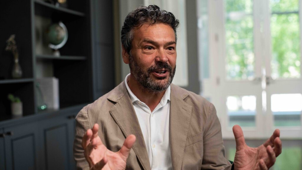 Man in beige jacket pictures talking with his hands opened - this is John Cooper from BAR Technologies