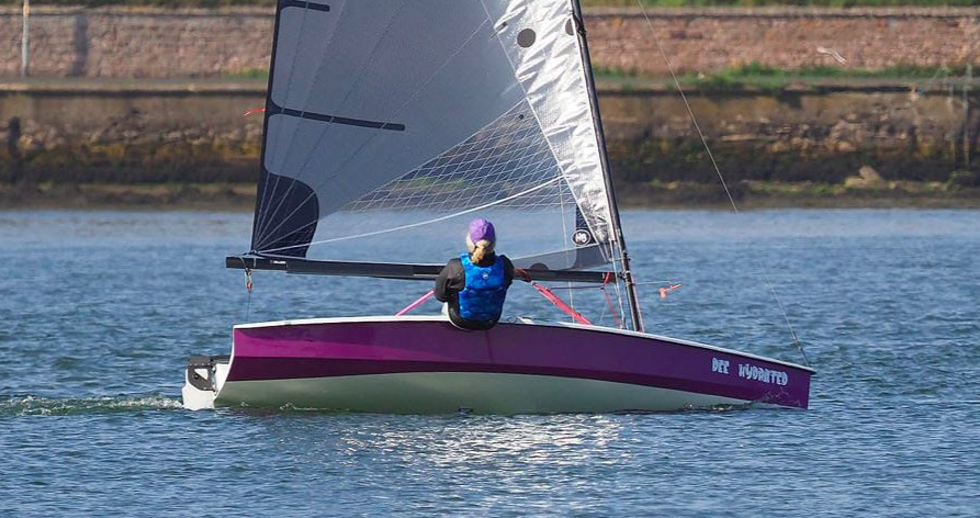 Beiboot - Zenith - mit lila Rumpf, von der Seite gesehen, mit Matrose auf dem Wasser