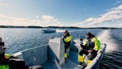 Males sit in boat and look at another boat which is on foils