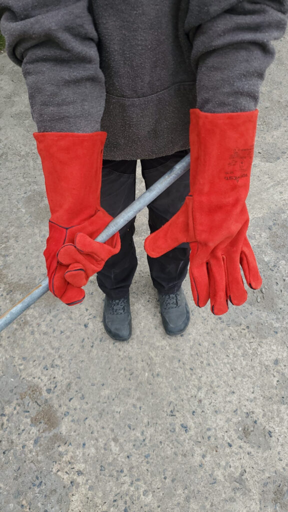a boatbuilder holds out their hands to demonstrate how large the bright red gloves are on them
