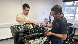 Two men work on a marine V8 engine in training room