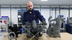 a technician behjnd a bench with 3D printed items on it for use in marine sector