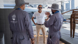 two men on yacht in grey overalls with another man in a white polo