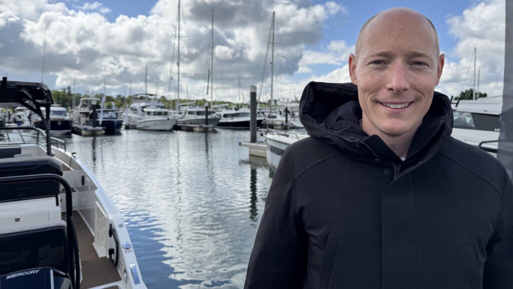 Oliver Lanza stands in black coat in a marina