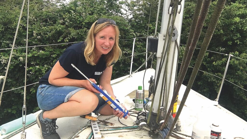 A sailor squats on a yacht bow to perform repairs