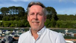 man smiles at camera with harbour in background