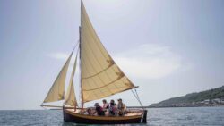 a group of people sit in a wooden sailing boat as it is launched for first time
