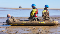 man stuck in mud with two coastguard personnel on hand