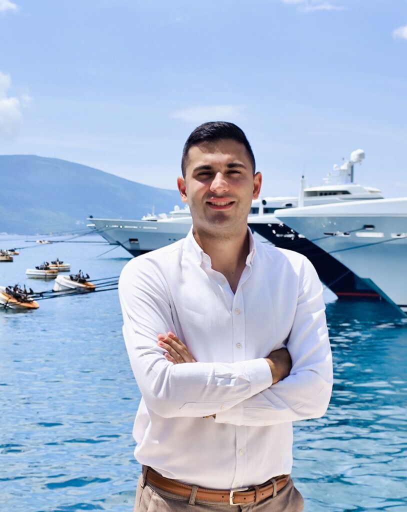 Man in shirt with superyacht behind him