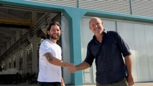 Two men shaking hands in front of boat factory