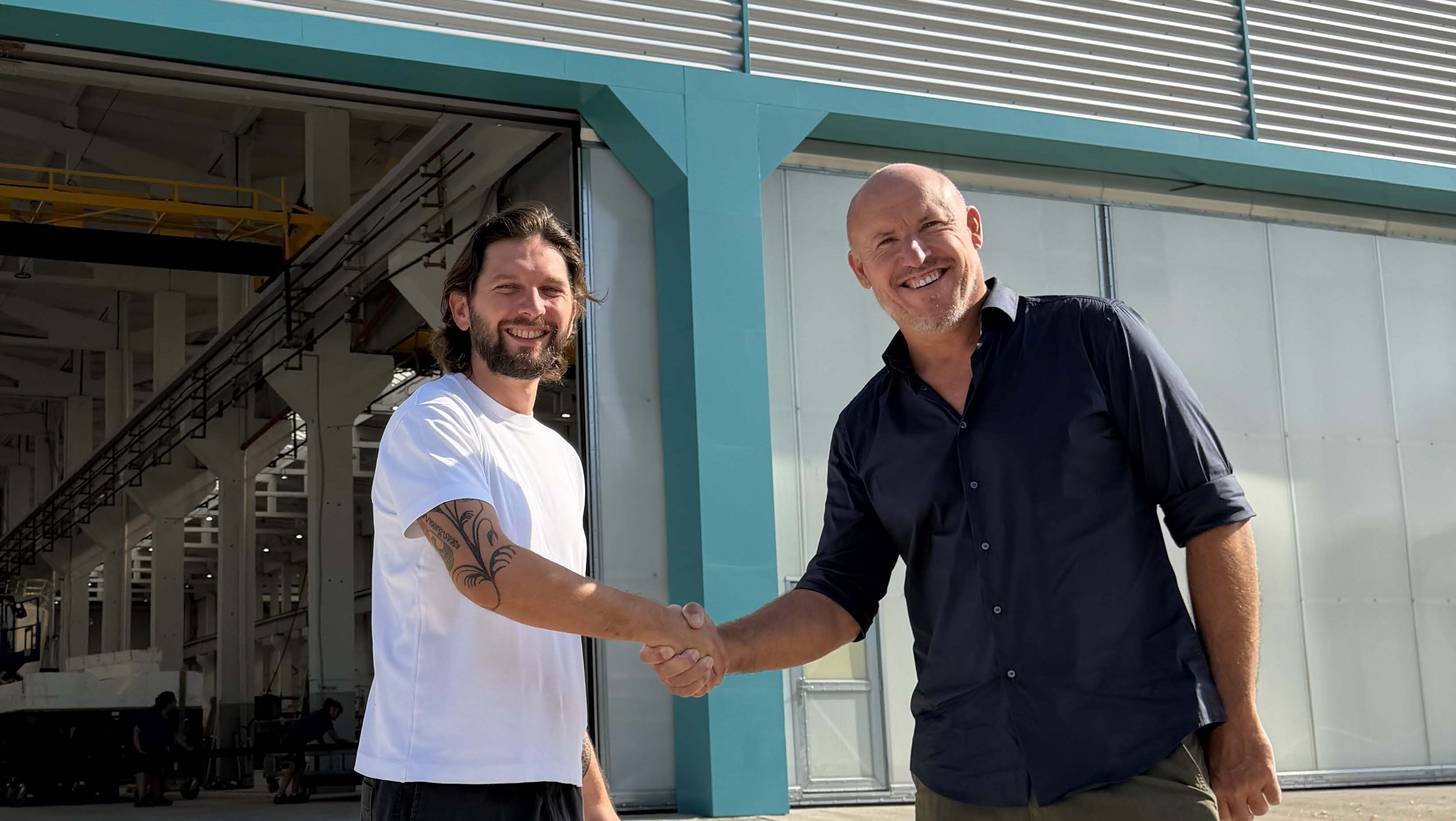 Two men shaking hands in front of boat factory