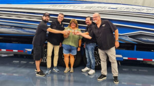 Five people raise glasses in front of an Outerlimits performance boat inside the company’s factory