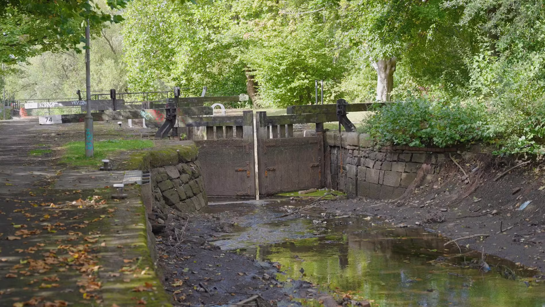 A drained UK canal lock with exposed muddy banks and low water levels during drought.